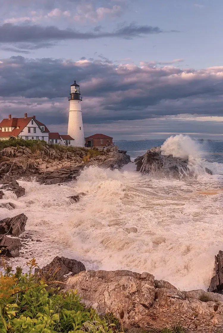 Storm surge crashing against the base of a coastal lighthouse tower