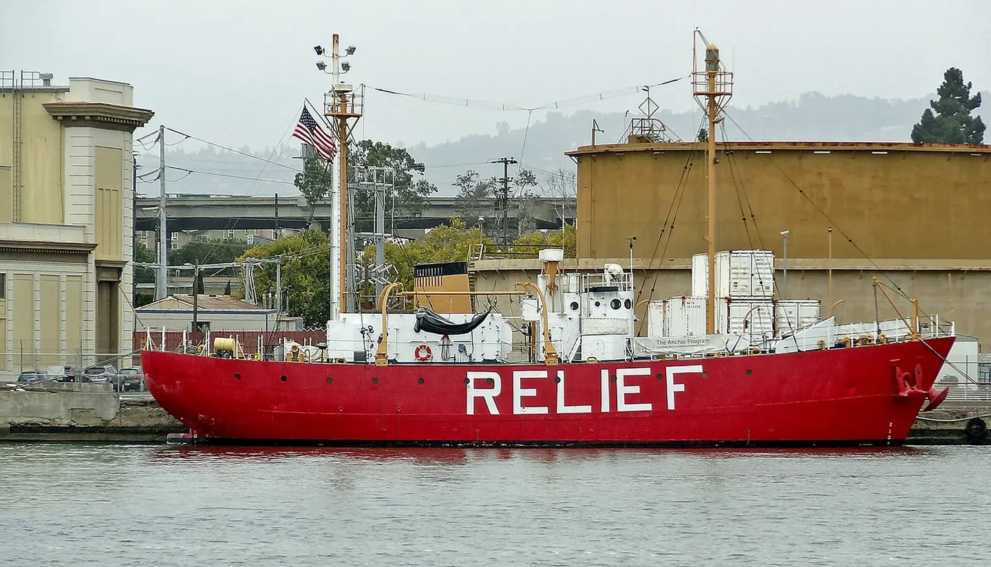 A red-hulled lightship riding at anchor, its beacon lantern atop the mast